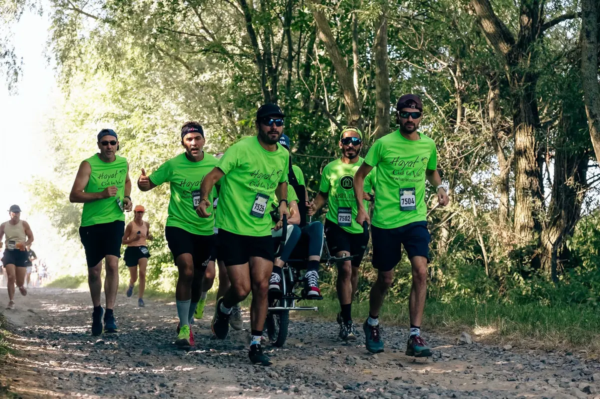 Pousseurs bénévoles de l'association sur un sentier de trail avec une joëlette